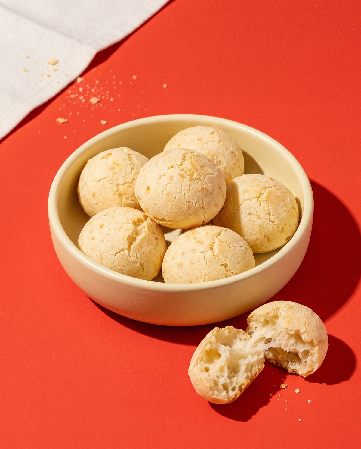 Pães de queijo coquetel dourados em prato de cerâmica sob luz solar